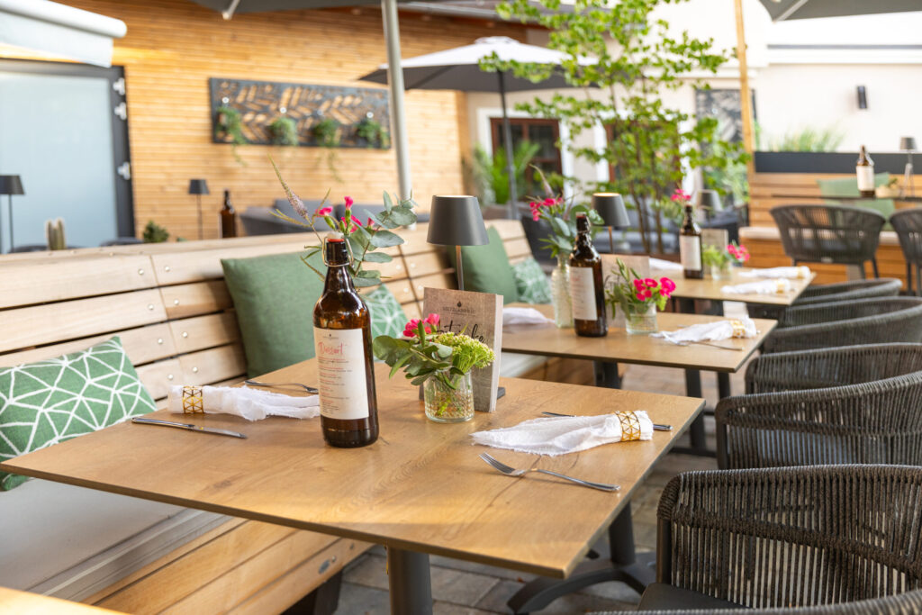 Gedeckte Holztische mit Blumen und grünen Sitzpolstern auf der Terrasse des Metzgerbräu.